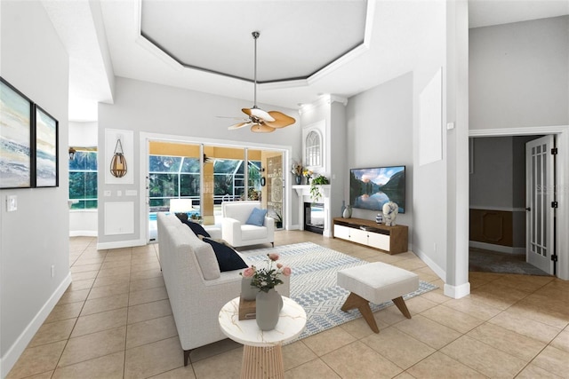 living room with a raised ceiling, light tile patterned floors, baseboards, and ceiling fan