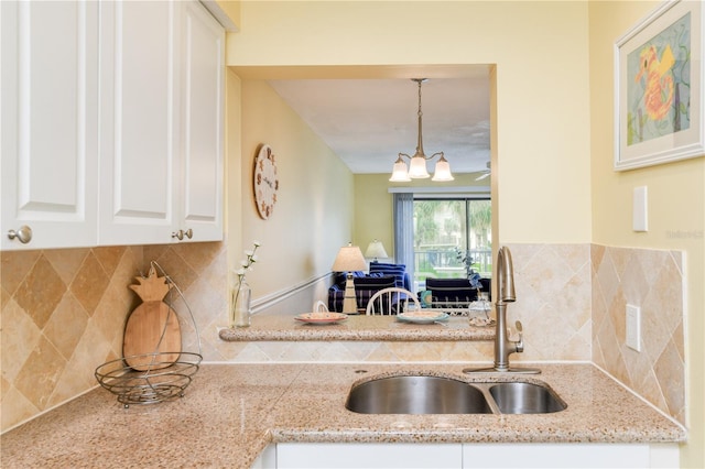 kitchen with tasteful backsplash, sink, light stone countertops, hanging light fixtures, and white cabinets