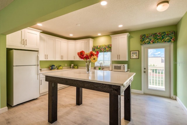 kitchen with white appliances, light hardwood / wood-style flooring, a textured ceiling, sink, and white cabinets