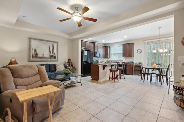 tiled living room with ceiling fan with notable chandelier and a tray ceiling