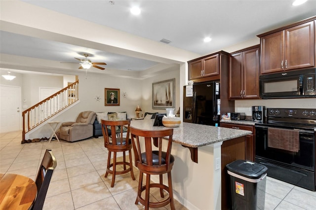 kitchen featuring a kitchen island, a kitchen breakfast bar, black appliances, light tile patterned floors, and ceiling fan