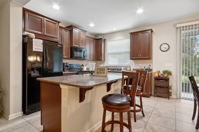 kitchen with black appliances, a kitchen island, a wealth of natural light, and stone counters