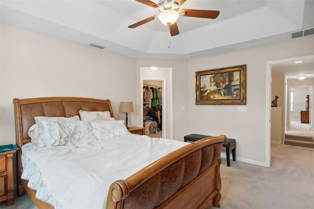 carpeted bedroom with a raised ceiling, a walk in closet, ceiling fan, and a closet