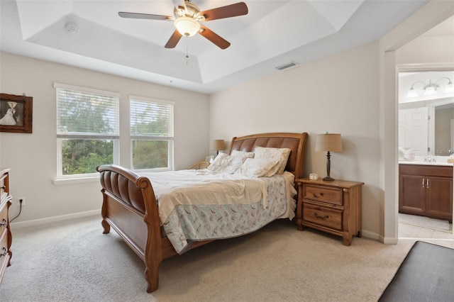 bedroom with light colored carpet, ceiling fan, ensuite bath, and a tray ceiling