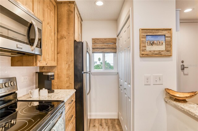 kitchen with a textured ceiling, light stone countertops, hardwood / wood-style floors, appliances with stainless steel finishes, and decorative backsplash