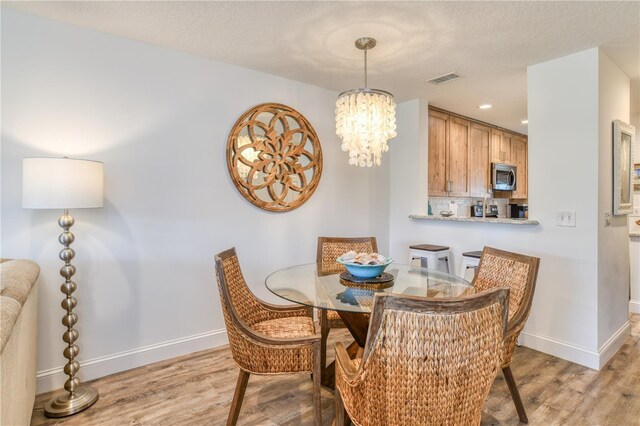 dining space with a textured ceiling, an inviting chandelier, and light hardwood / wood-style floors