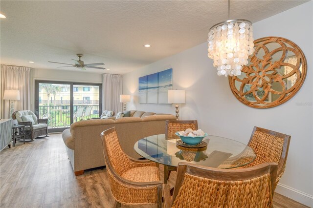 dining room with ceiling fan with notable chandelier, a textured ceiling, and wood-type flooring