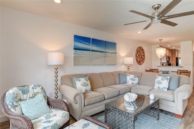 living room with ceiling fan with notable chandelier, light wood-type flooring, and a textured ceiling