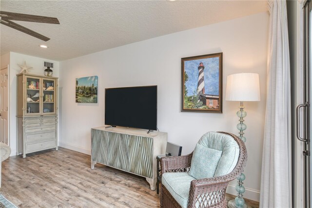 living area featuring a textured ceiling, light hardwood / wood-style flooring, and ceiling fan