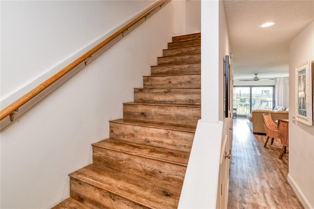 stairway featuring ceiling fan, hardwood / wood-style flooring, and a textured ceiling