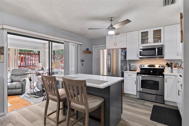 kitchen with a textured ceiling, appliances with stainless steel finishes, light hardwood / wood-style floors, white cabinetry, and ceiling fan