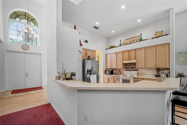 kitchen featuring a breakfast bar area, light brown cabinetry, stainless steel refrigerator with ice dispenser, light hardwood / wood-style flooring, and white range with electric cooktop