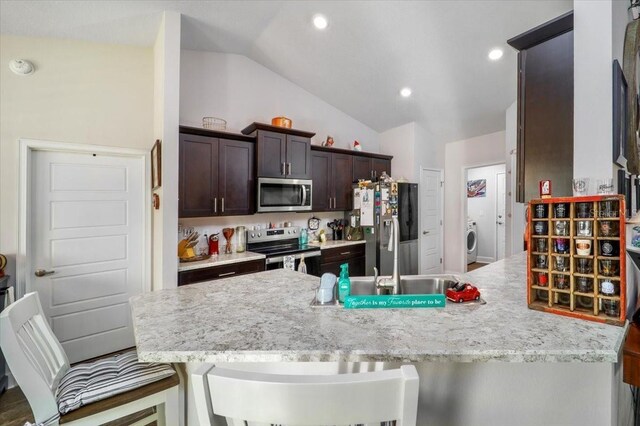 kitchen featuring dark brown cabinets, appliances with stainless steel finishes, a kitchen bar, lofted ceiling, and light stone counters