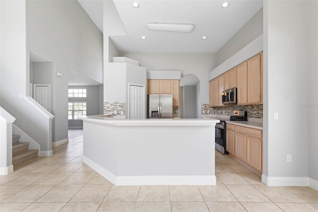 kitchen with backsplash, light brown cabinetry, a towering ceiling, appliances with stainless steel finishes, and light tile patterned flooring