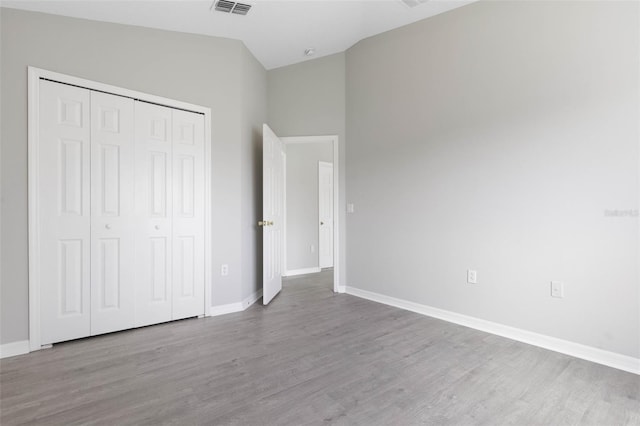 unfurnished bedroom with vaulted ceiling, a closet, and light hardwood / wood-style floors