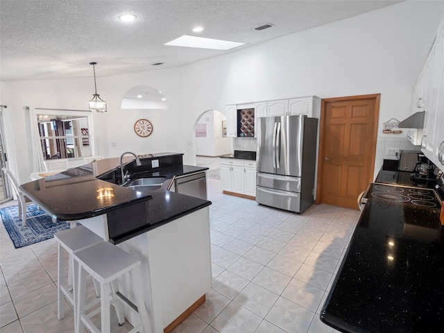 kitchen with a kitchen island with sink, stainless steel appliances, sink, a skylight, and white cabinets