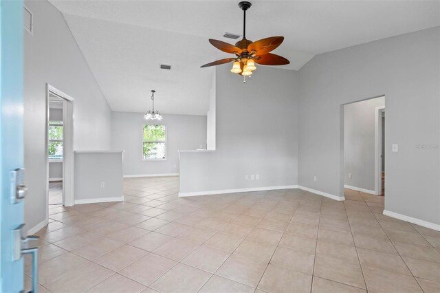 tiled empty room featuring ceiling fan with notable chandelier and vaulted ceiling