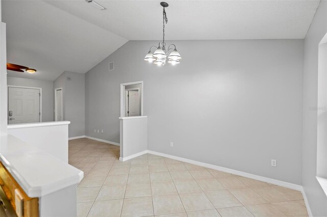 tiled spare room featuring lofted ceiling and a chandelier