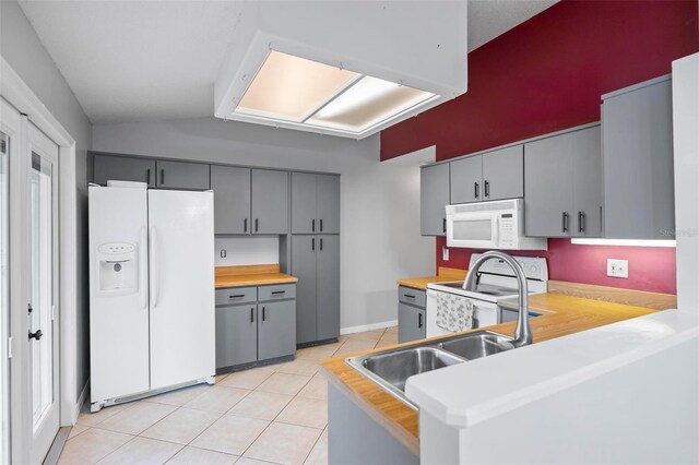 kitchen featuring white appliances, kitchen peninsula, gray cabinetry, vaulted ceiling, and light tile patterned flooring