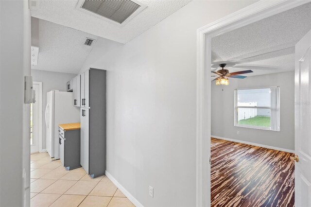 hall with vaulted ceiling, a textured ceiling, and light tile patterned floors