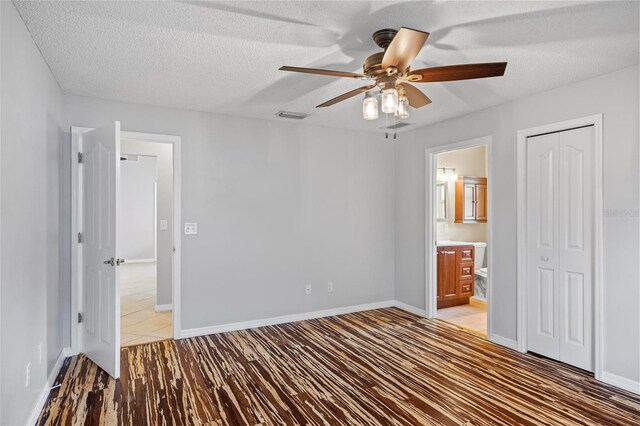 unfurnished bedroom with a textured ceiling, a closet, ensuite bath, hardwood / wood-style flooring, and ceiling fan