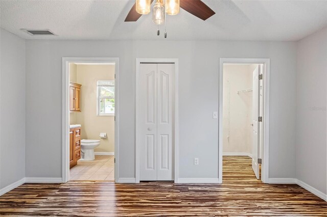 unfurnished bedroom featuring a textured ceiling, hardwood / wood-style floors, ensuite bathroom, and ceiling fan