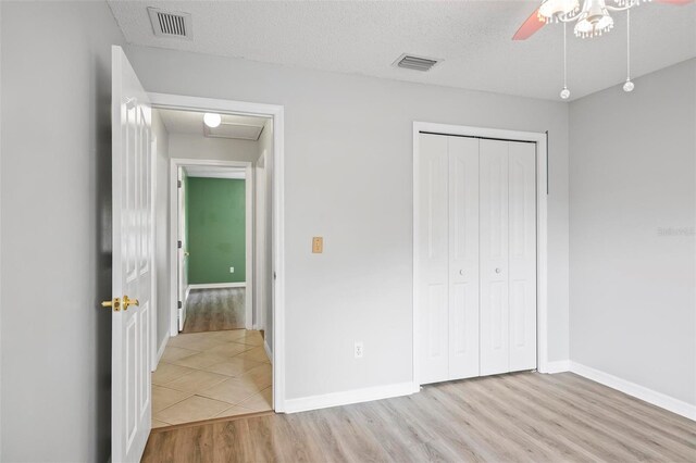 unfurnished bedroom featuring a textured ceiling, light hardwood / wood-style flooring, ceiling fan, and a closet