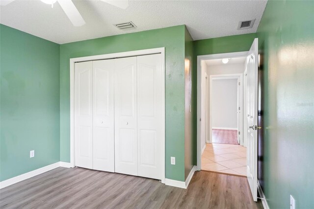 unfurnished bedroom with a textured ceiling, light hardwood / wood-style flooring, ceiling fan, and a closet