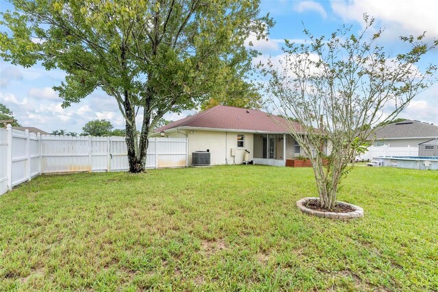 rear view of house with central AC and a lawn