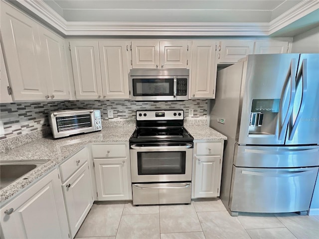 kitchen featuring tasteful backsplash, white cabinetry, appliances with stainless steel finishes, ornamental molding, and light stone countertops