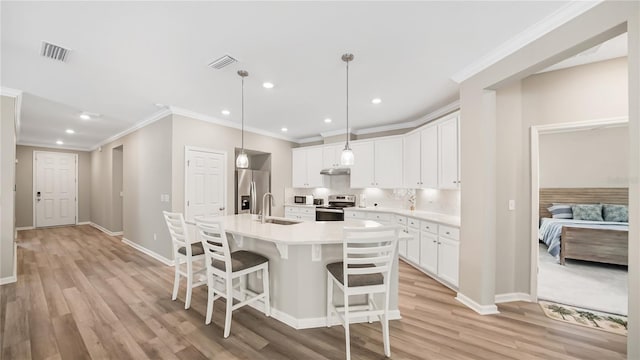 kitchen featuring light wood-type flooring, stainless steel appliances, an island with sink, and white cabinetry