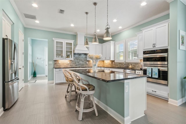 kitchen featuring visible vents, premium range hood, a breakfast bar, stainless steel appliances, and white cabinetry