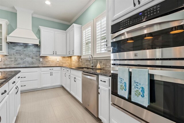 kitchen with white cabinets, appliances with stainless steel finishes, dark stone countertops, and premium range hood