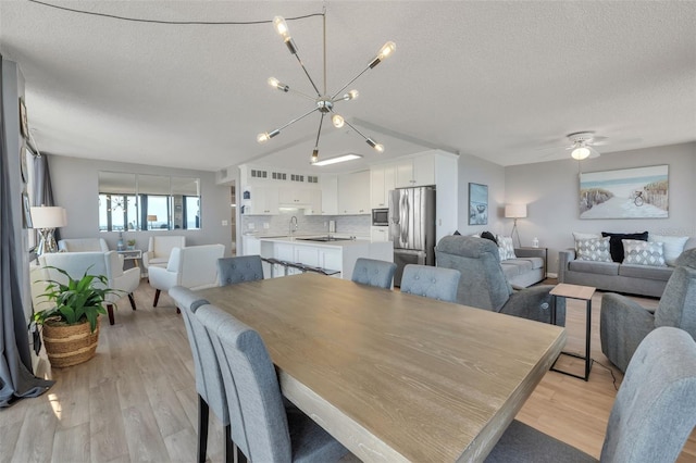 dining area with a textured ceiling, ceiling fan with notable chandelier, and light hardwood / wood-style floors