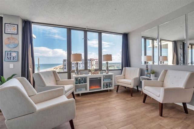 living room featuring light wood-type flooring, a water view, a textured ceiling, and floor to ceiling windows