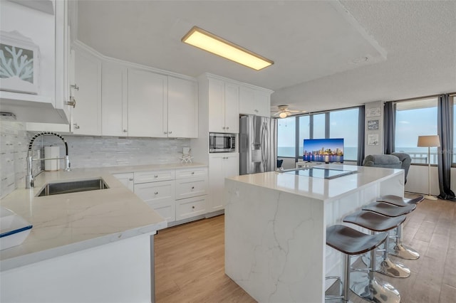 kitchen with sink, a kitchen island, white cabinetry, stainless steel appliances, and light hardwood / wood-style floors