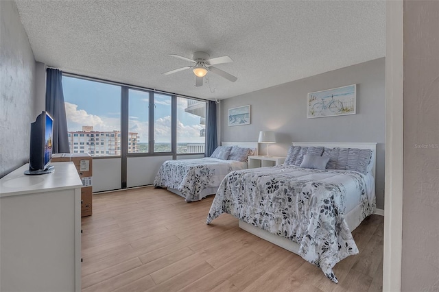 bedroom with light hardwood / wood-style flooring, ceiling fan, a wall of windows, and a textured ceiling