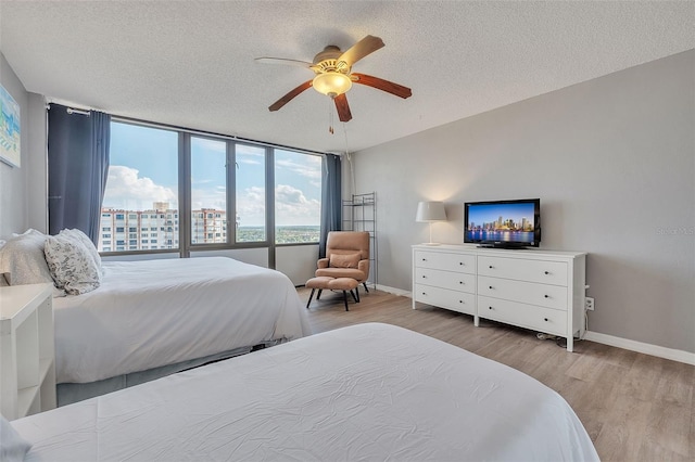 bedroom featuring ceiling fan, a textured ceiling, expansive windows, and wood-type flooring