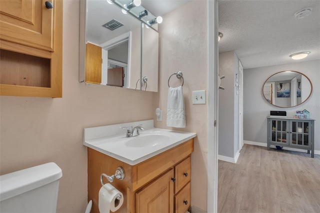 bathroom with wood-type flooring, vanity, toilet, and a textured ceiling