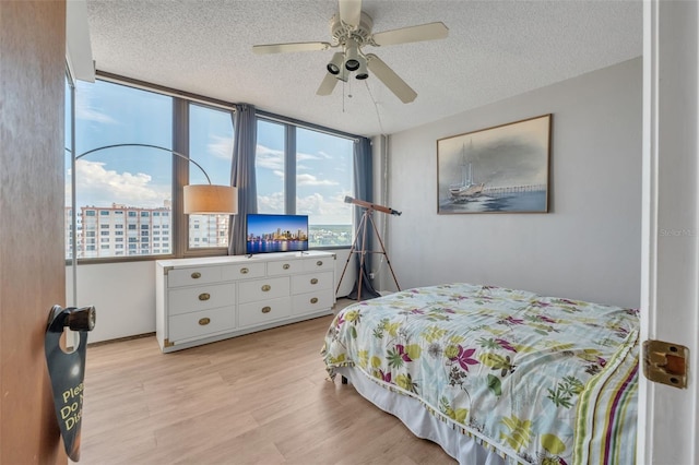 bedroom with ceiling fan, a wall of windows, a textured ceiling, and light hardwood / wood-style flooring