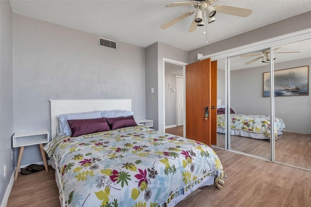 bedroom featuring light wood-type flooring, a textured ceiling, ceiling fan, and a closet