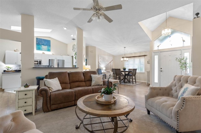 living room with ceiling fan with notable chandelier, a textured ceiling, light hardwood / wood-style flooring, and a skylight