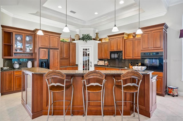 kitchen with black appliances, a raised ceiling, a center island, and decorative light fixtures