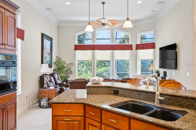 kitchen featuring hanging light fixtures, oven, light stone counters, sink, and ceiling fan