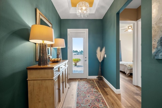 doorway with light hardwood / wood-style flooring, a tray ceiling, and ceiling fan with notable chandelier