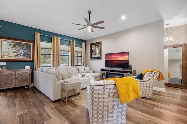 living room with light wood-type flooring, ceiling fan with notable chandelier, and a fireplace