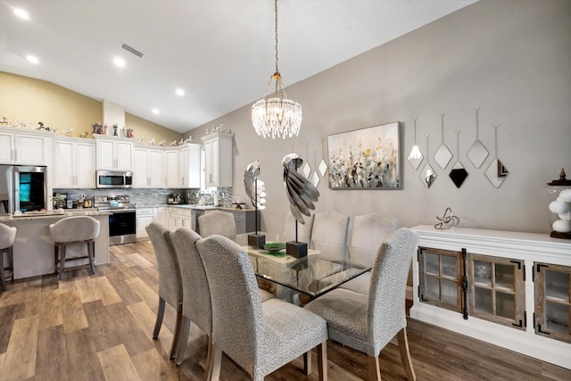 dining area with a notable chandelier, vaulted ceiling, and hardwood / wood-style floors