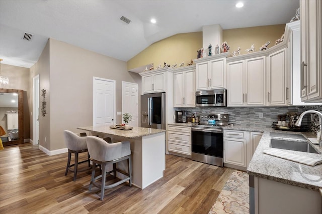 kitchen with lofted ceiling, sink, a kitchen island, light hardwood / wood-style flooring, and stainless steel appliances