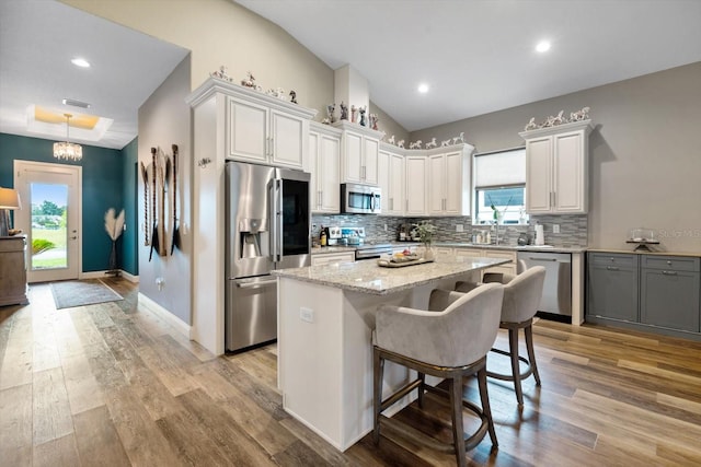 kitchen with appliances with stainless steel finishes, light hardwood / wood-style floors, vaulted ceiling, white cabinets, and a kitchen island