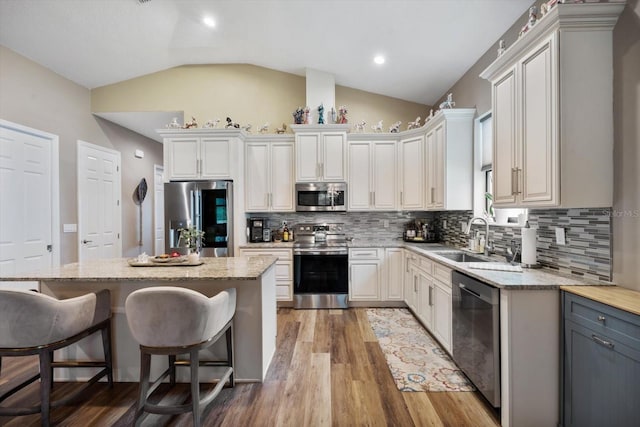 kitchen featuring appliances with stainless steel finishes, white cabinetry, lofted ceiling, a center island, and hardwood / wood-style flooring